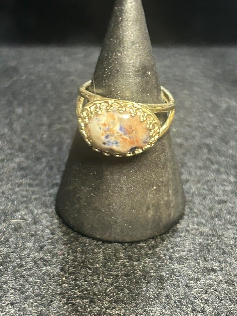 Gold ring with decorative stone on stand.